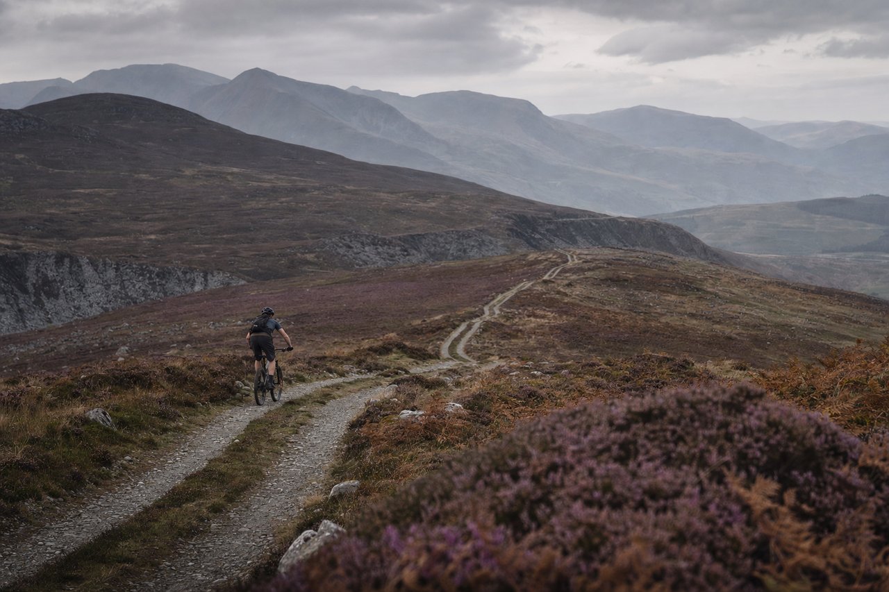 Mountain biker climbing a remote Welsh gravel track under moorland skies